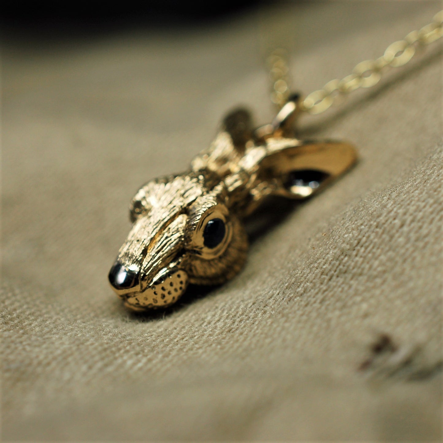Gold rabbit necklace. Gold hare pendant with green peridot eyes and a gold chain. Hand made to order in the UK. © Adrian Ashley